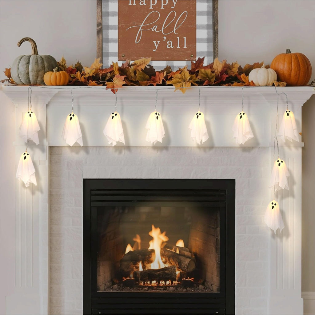 Halloween ghost string lights draped over a fireplace mantel with pumpkins and fall leaves