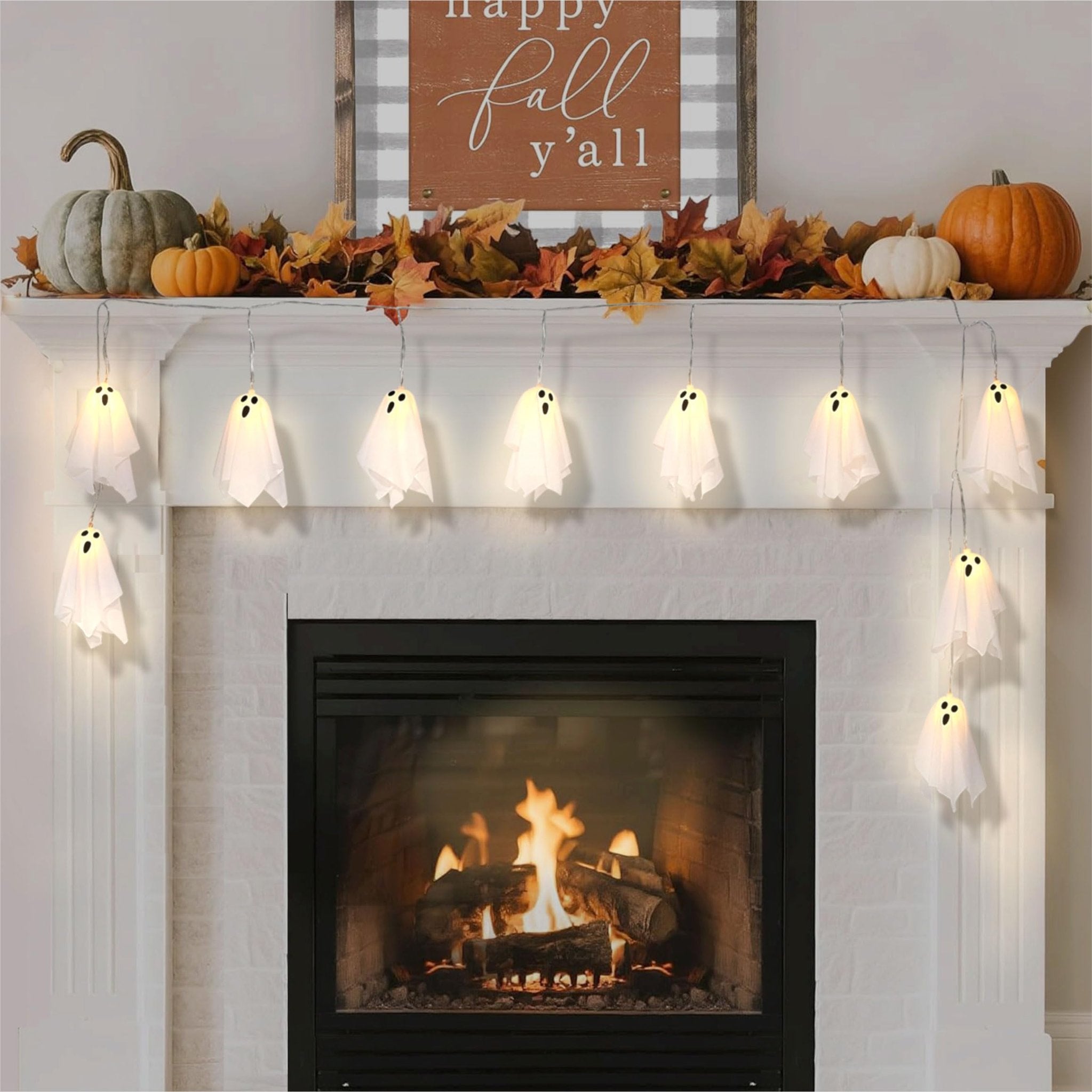 Halloween ghost string lights draped over a fireplace mantel with pumpkins and fall leaves