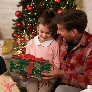 Father and daughter opening a Christmas gift in front of a decorated tree