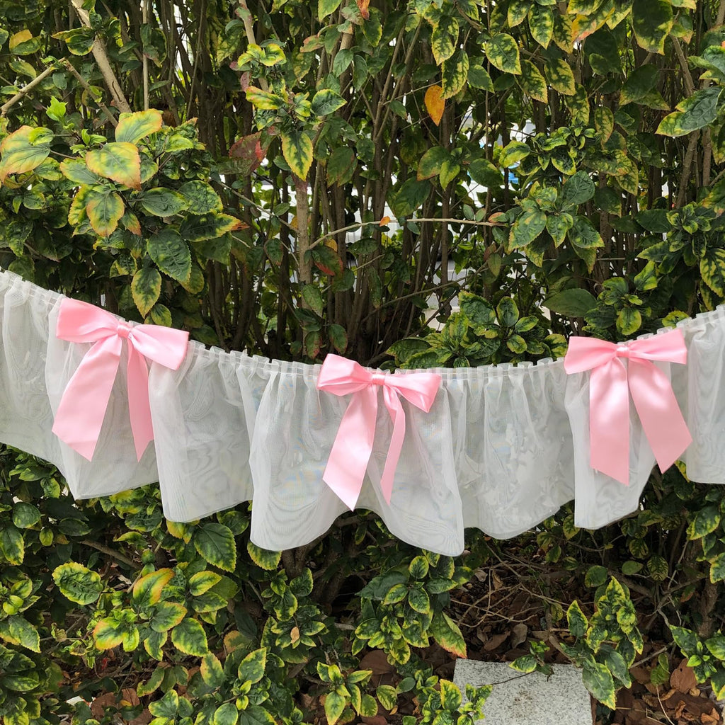 White lace banner with pink satin bows hanging in front of green foliage