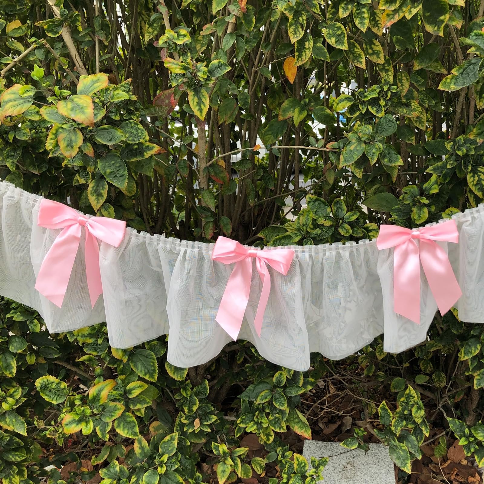 White lace banner with pink satin bows hanging in front of green foliage