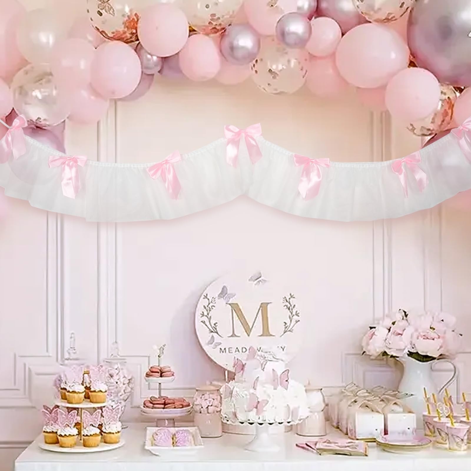 Pink and white lace and satin ribbon banner with bows, draped above a dessert table with cupcakes, cake, and balloons.