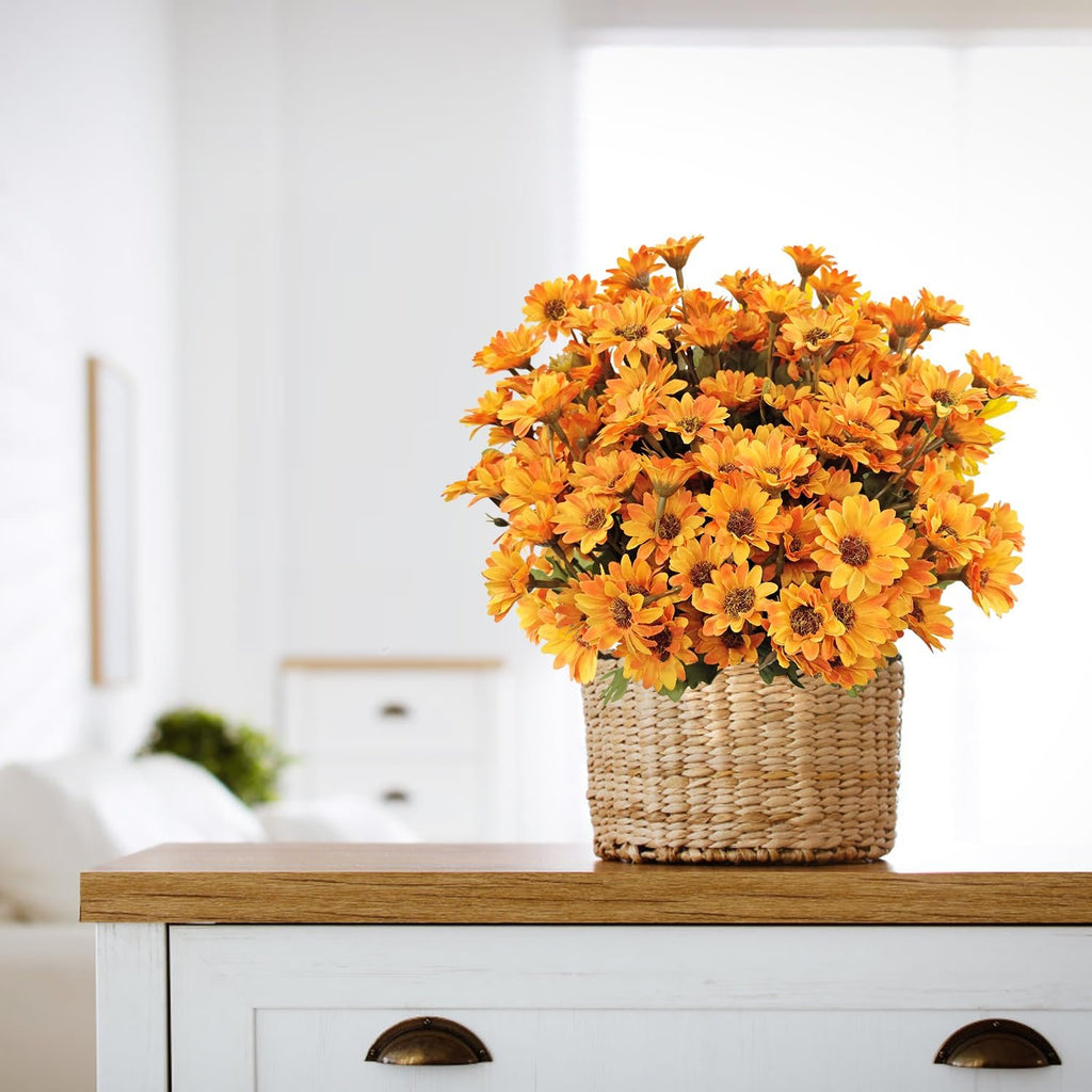 Basket of orange artificial mums on a wooden table in a bright room