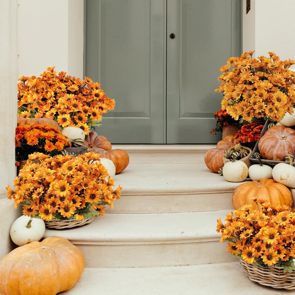 Artificial orange mums and pumpkins arranged on outdoor steps leading to a door.