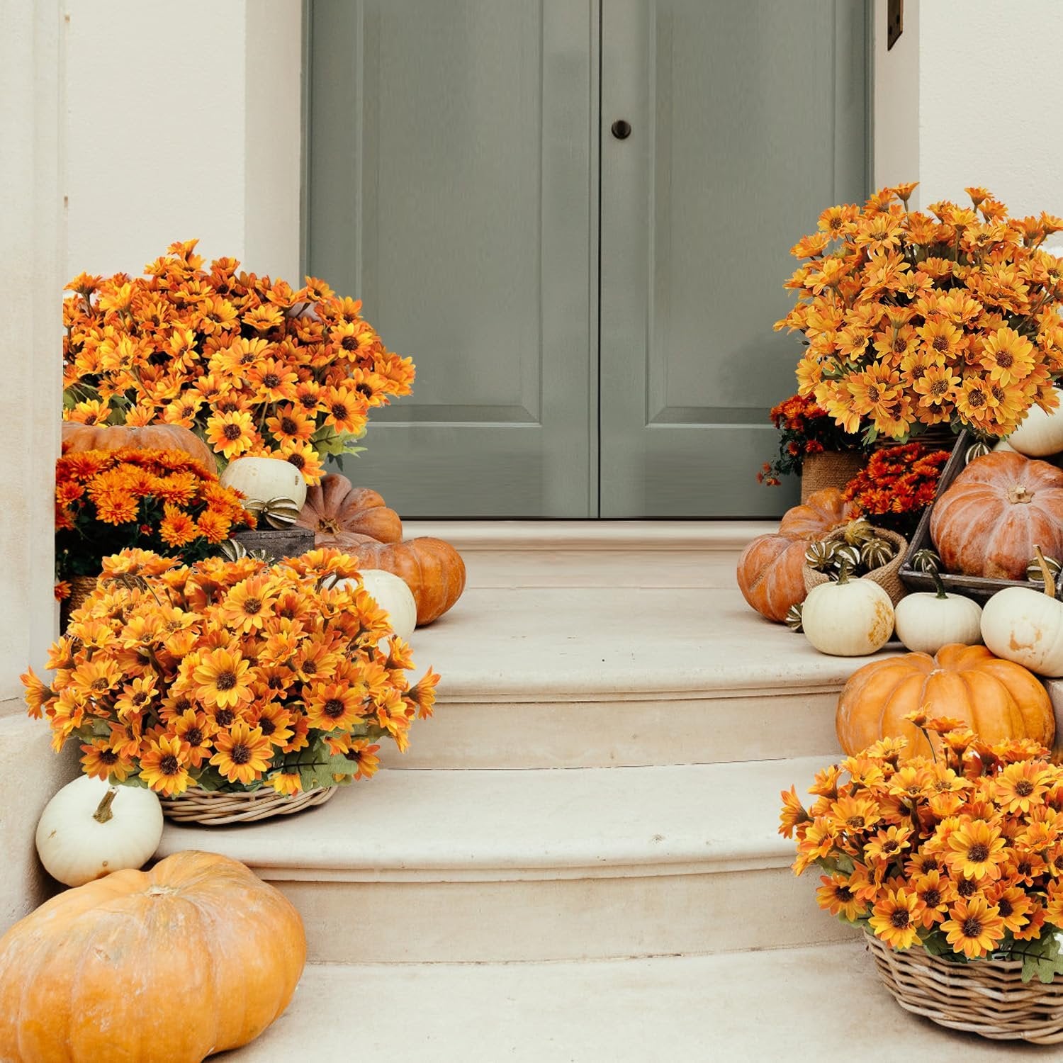 Artificial orange mums and pumpkins arranged on outdoor steps leading to a door.