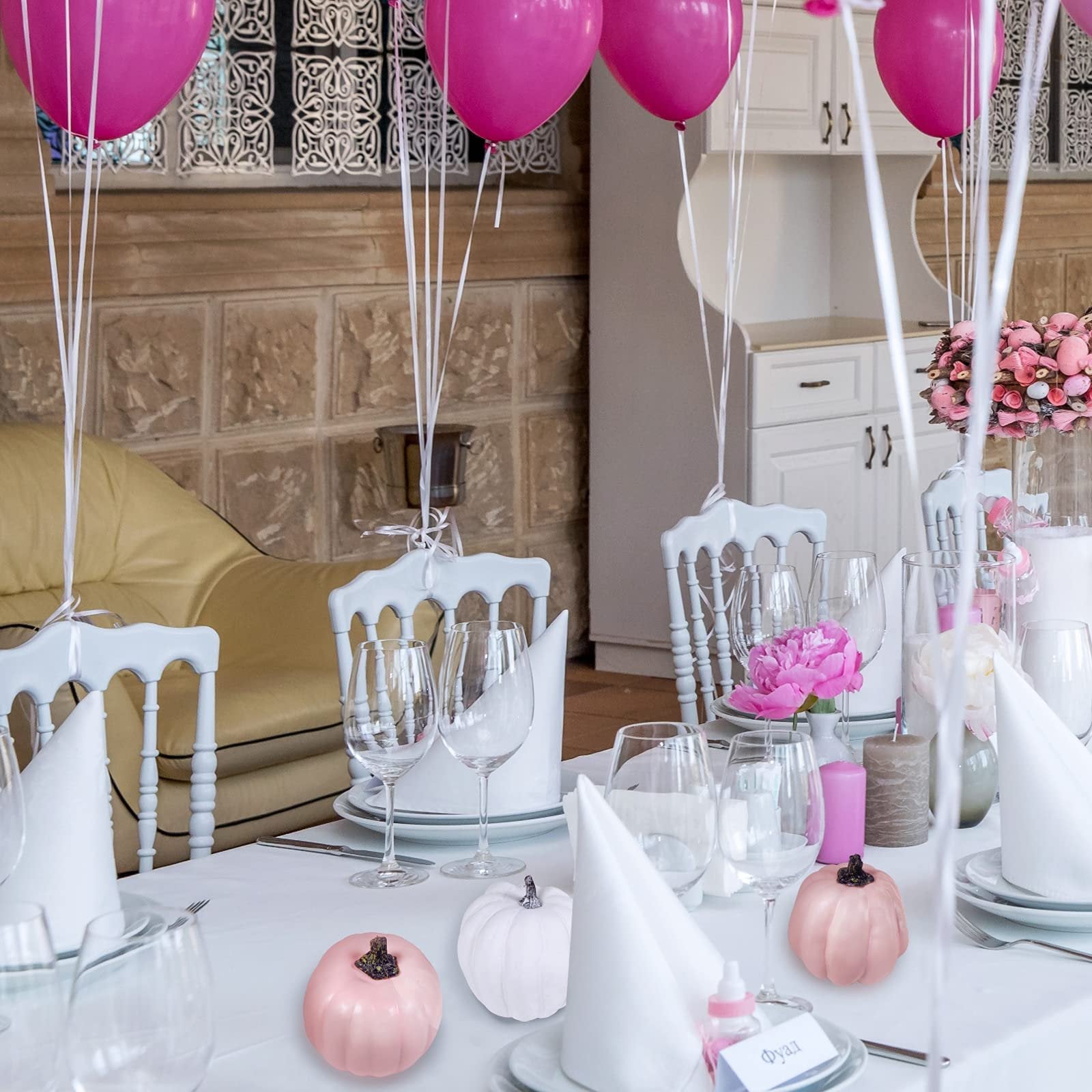 Assorted pink and white foam pumpkins arranged on a table with balloons and flowers