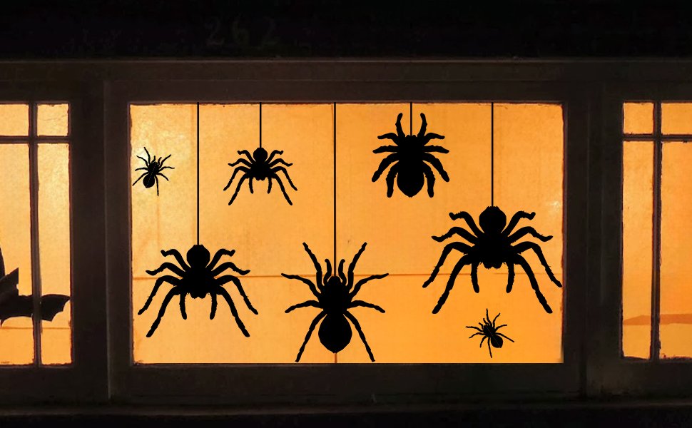 Seven black spider silhouette window clings hanging in a window with an orange glow behind them.