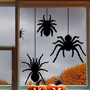 Halloween spider silhouette window clings hanging in a window with pumpkins below