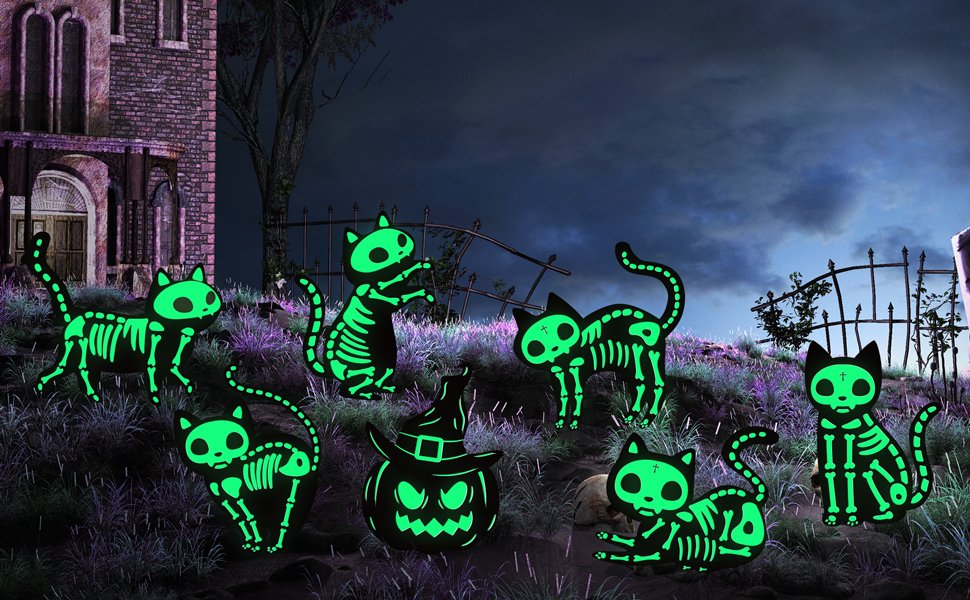 Seven glow-in-the-dark skeleton cat yard signs and one pumpkin sign arranged on a grassy hill with a spooky house and fence in the background.