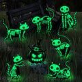 Seven glow-in-the-dark Halloween yard signs featuring skeleton cats and a pumpkin in a grassy, outdoor setting at night.