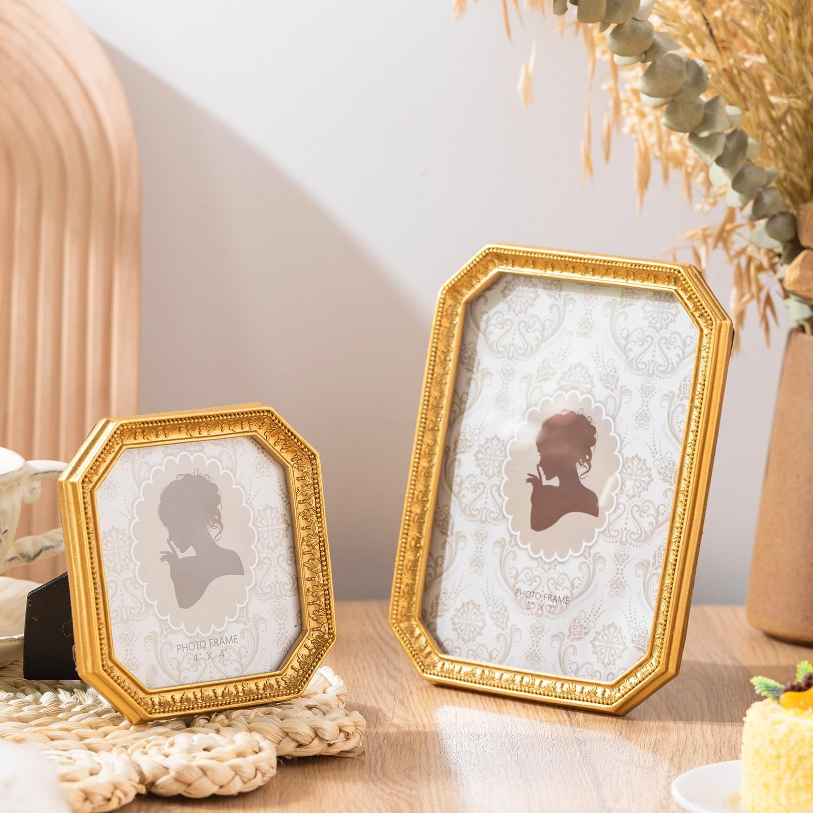 Two antique gold resin photo frames with ornate borders displayed on a wooden surface with decorative elements.
