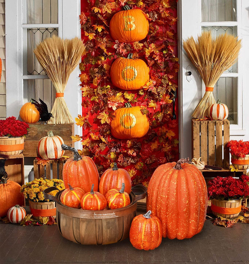 Fall harvest display with various artificial pumpkins, wheat bundles, and autumn leaves arranged on a porch.
