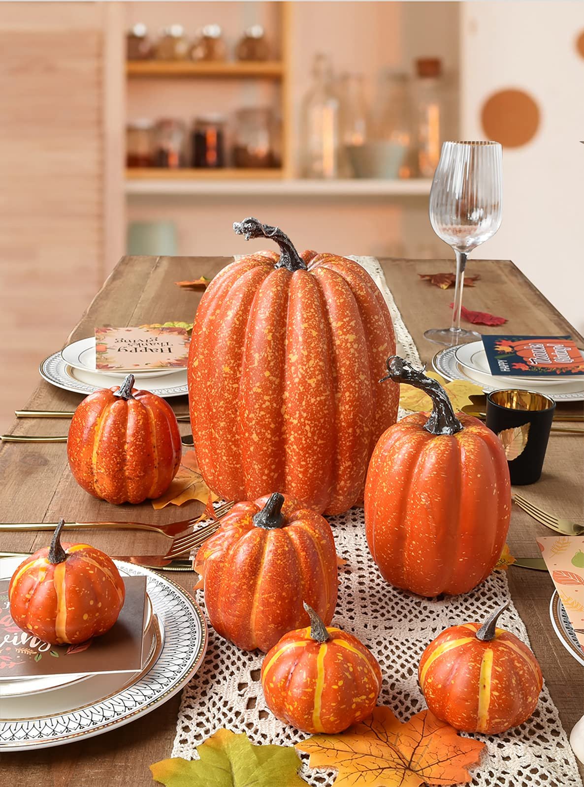 Set of seven artificial orange pumpkins arranged on a table with fall leaves and place settings.