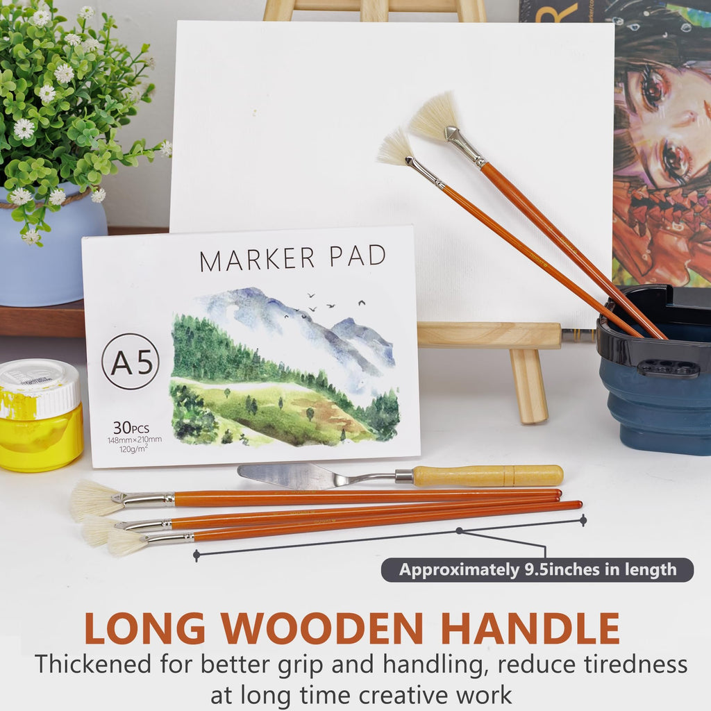 Fan paint brushes, marker pad, and art supplies arranged on a surface with a canvas in the background.