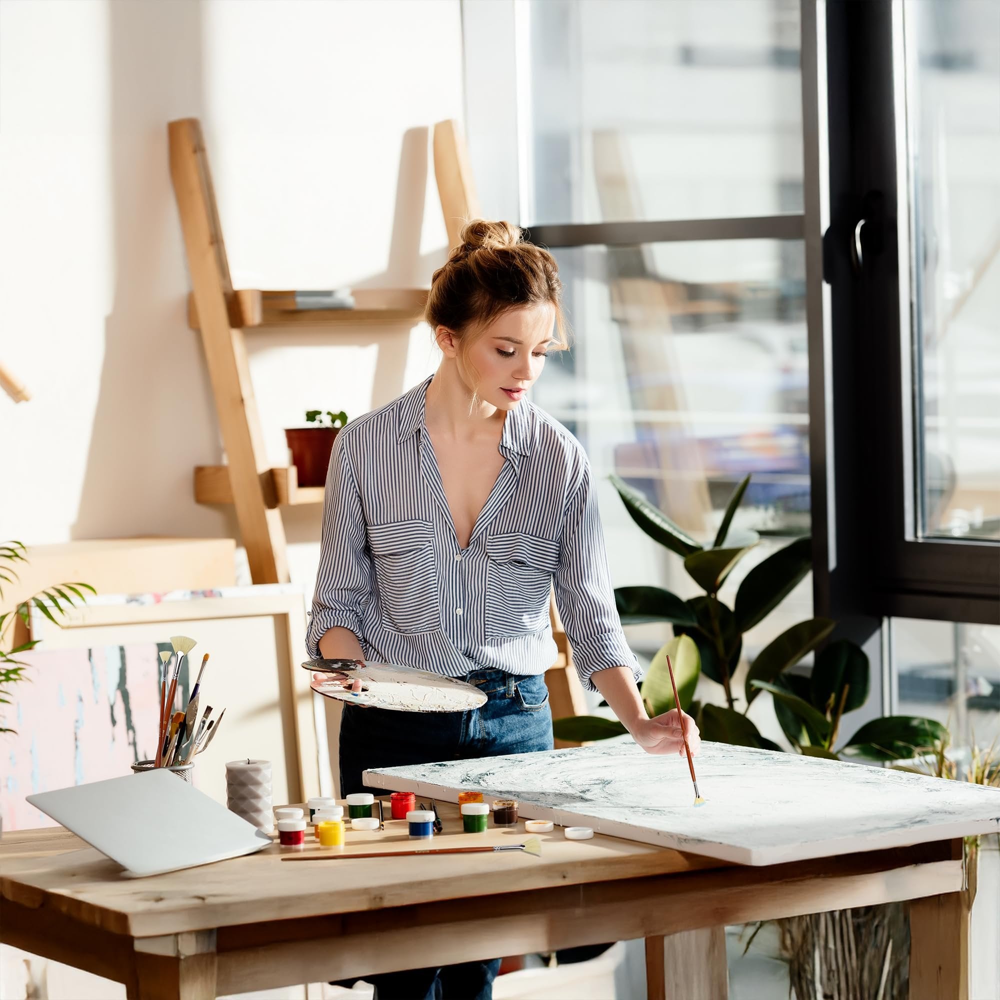 Woman painting on canvas with brush and palette in art studio with supplies