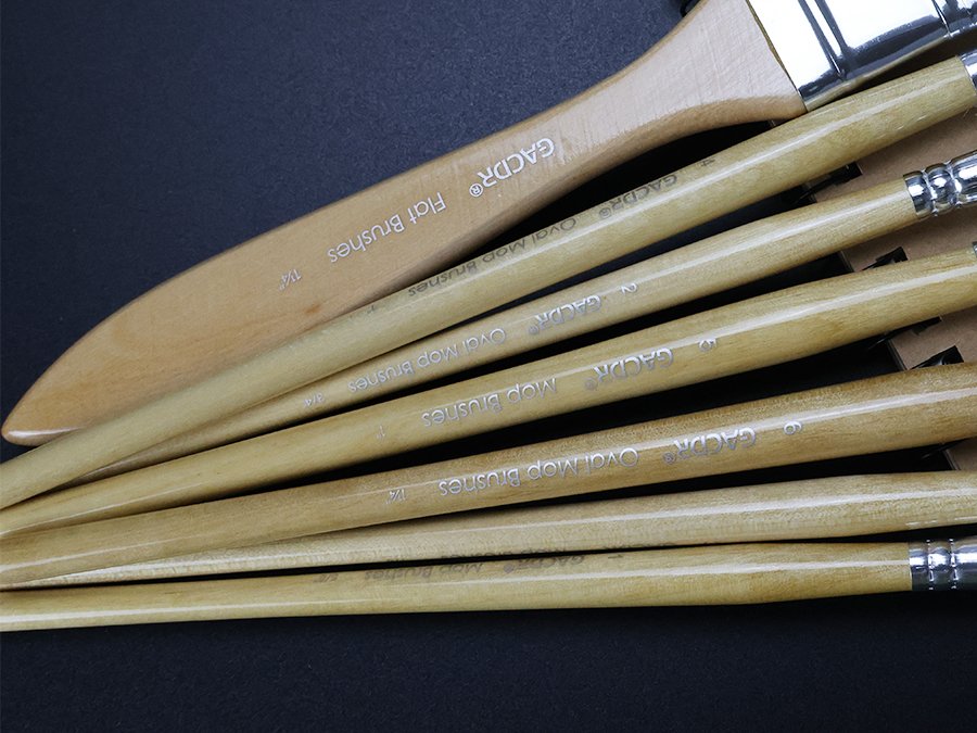 Close-up of a set of natural bristle gilding brushes with birch wood handles, showing various sizes and shapes.