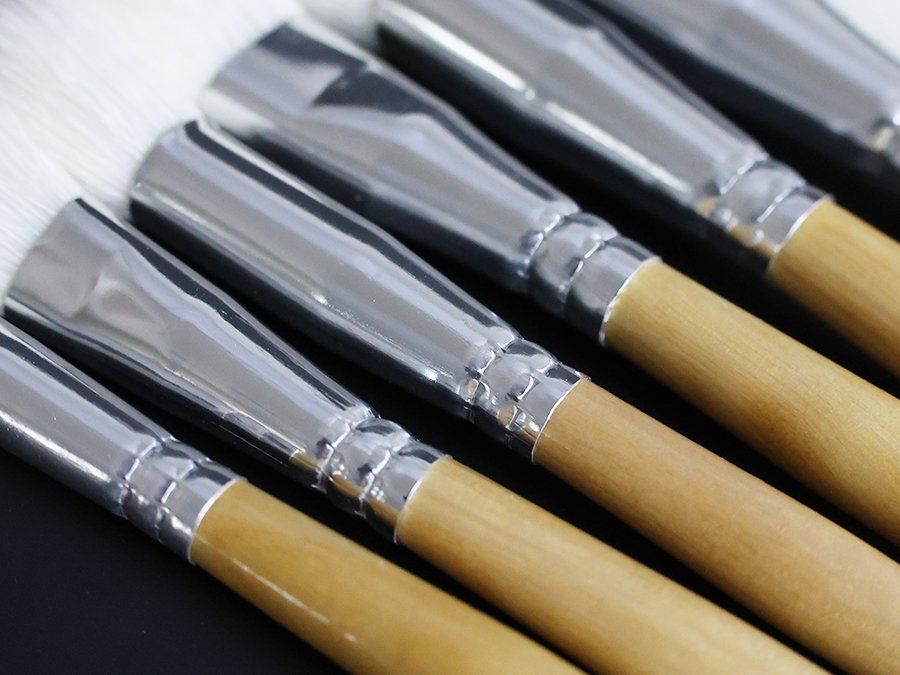 Close-up of a set of seven goat hair gilding brushes with natural bristles and birch wood handles, angled view.