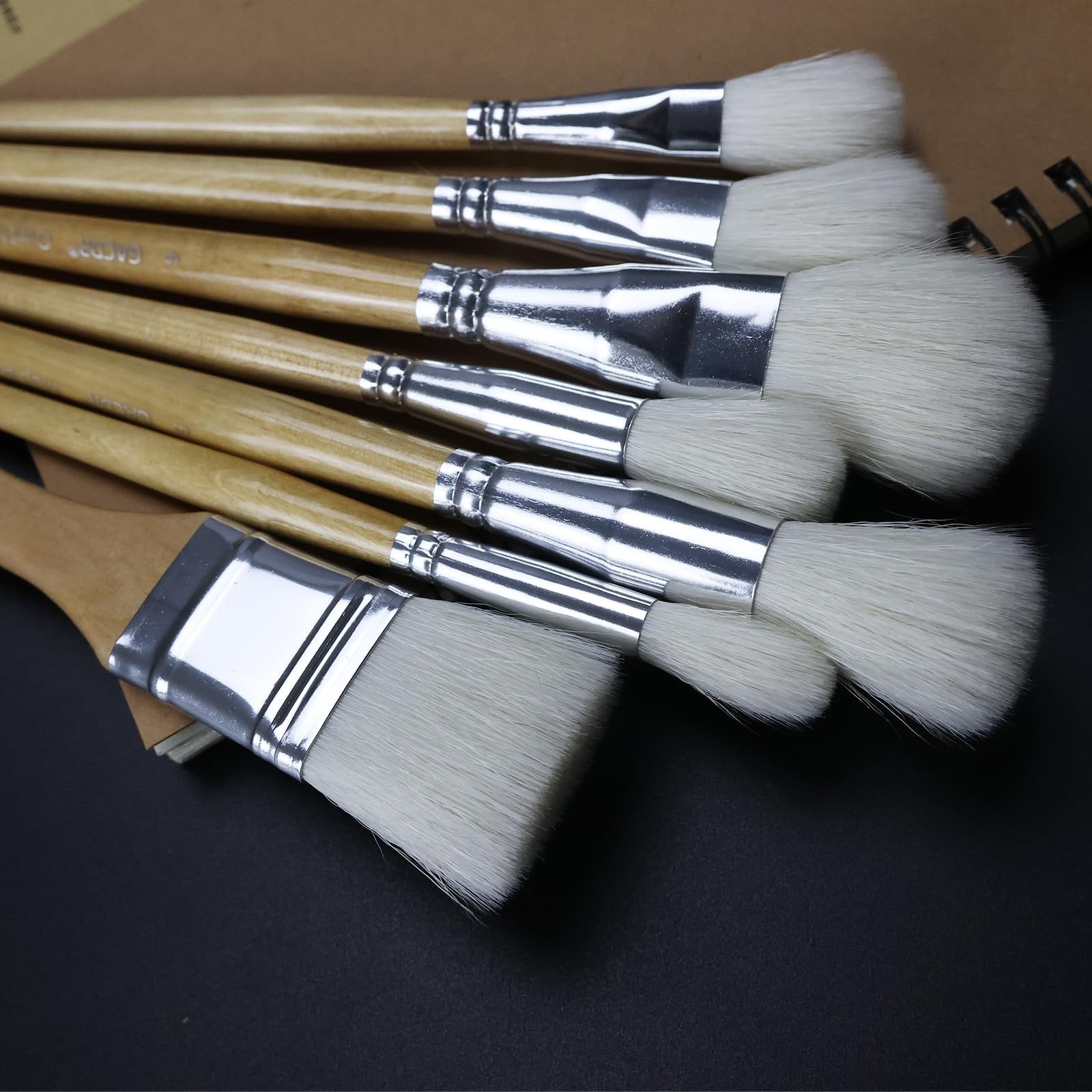 Set of seven goat hair gilding brushes with birch wood handles and silver ferrules, fanned out on a dark surface.