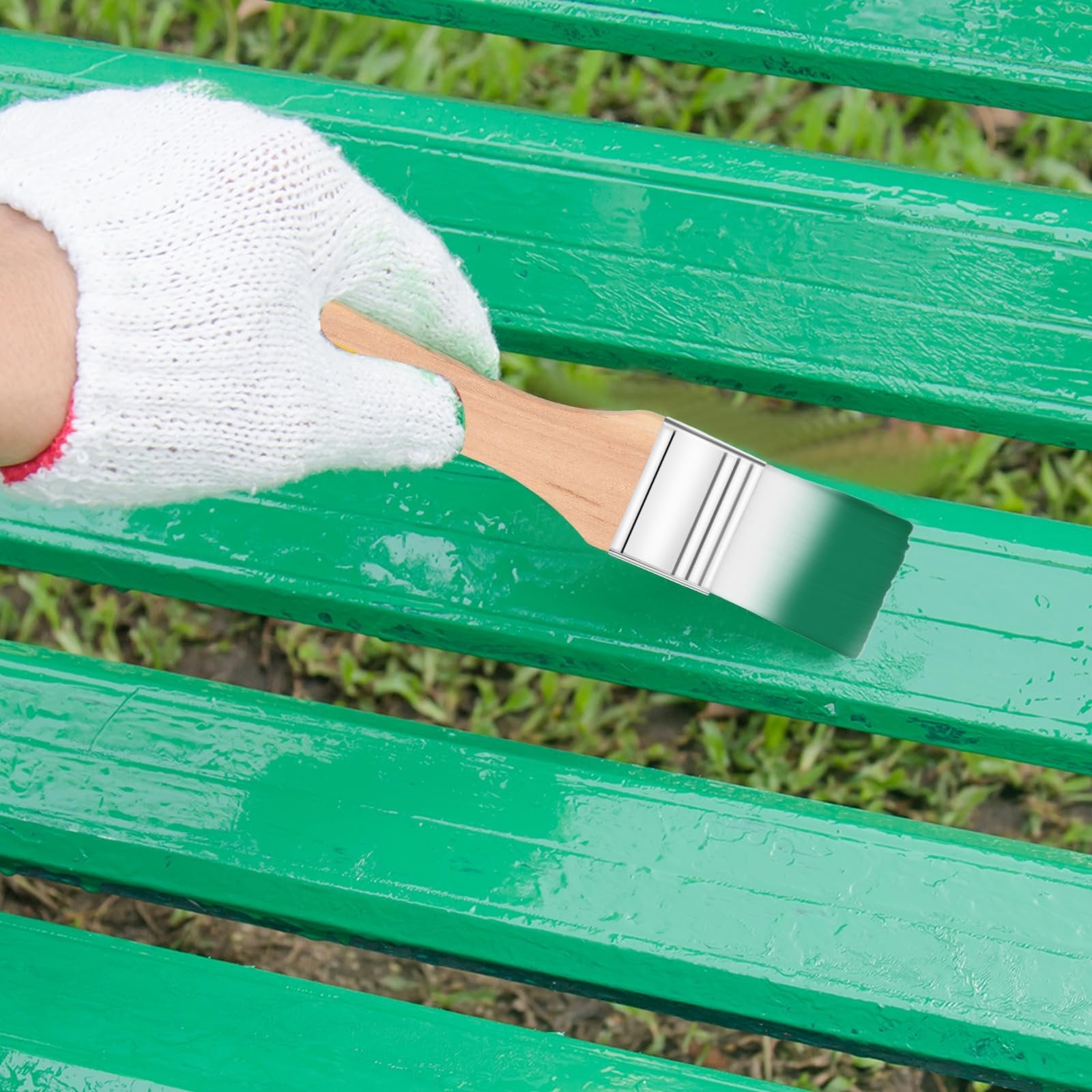 Gloved hand holding a paintbrush applying green paint to a wooden bench