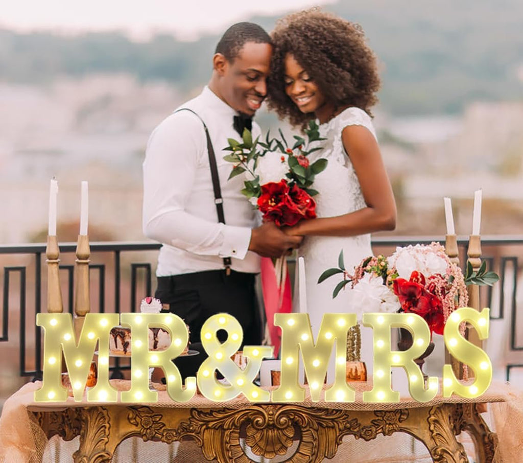 Wedding couple posing with illuminated "MR & MRS" marquee letters on a table