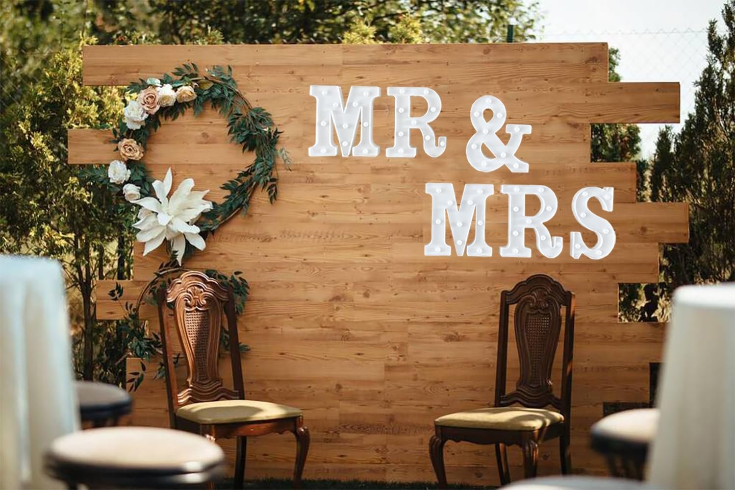LED "MR & MRS" sign with decorative wreath and chairs against a wooden wall backdrop