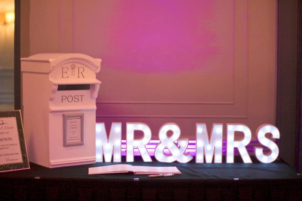 White illuminated "MR & MRS" sign and a white post box with "POST" text, set up for a wedding.