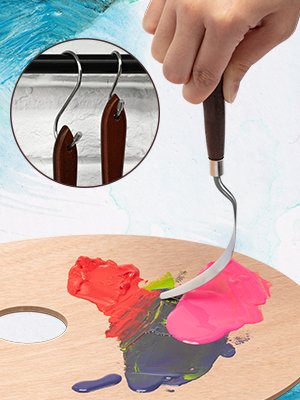 Artist's hand holding a palette knife, mixing red and pink paints on a wooden palette. Inset shows two palette knives hanging on hooks.