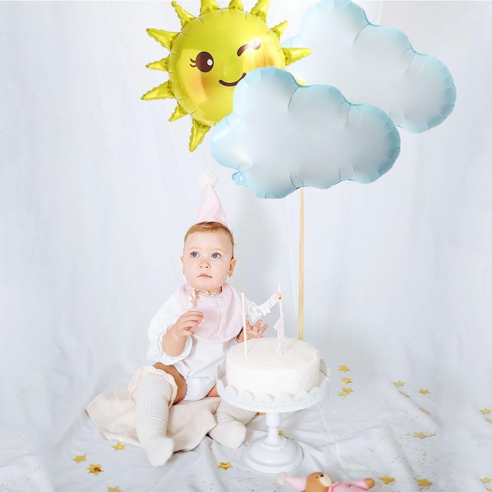 Baby girl in party hat and bib sits by cake with sun and cloud balloons overhead