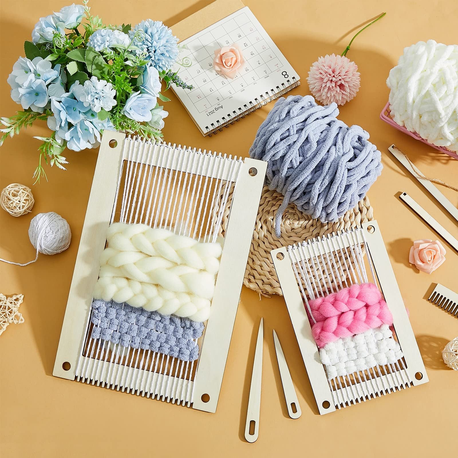 Two wooden weaving looms with yarn in progress, surrounded by yarn balls, flowers, and weaving tools on a tan background.