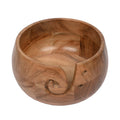 Acacia wood yarn bowl with a carved swirl and two small holes on the side, shown from a 3/4 angle on a white background.