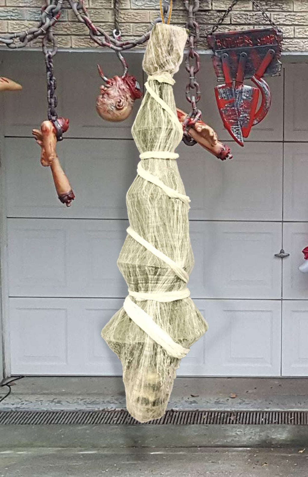 Hanging Halloween prop wrapped in gauze with white cloth strips, suspended by chains with severed body parts and a butcher shop sign.