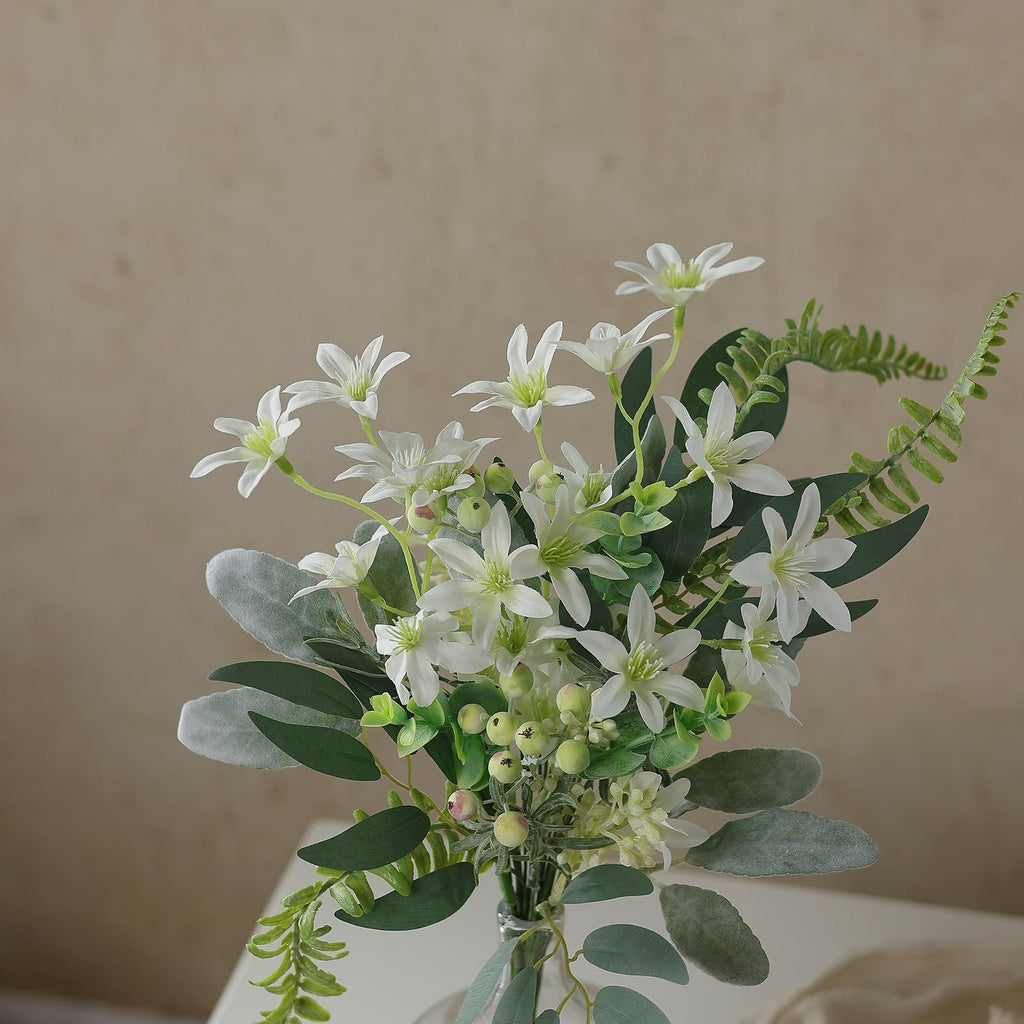 Artificial greenery stems bouquet with white flowers, green leaves, and berries in a clear vase.