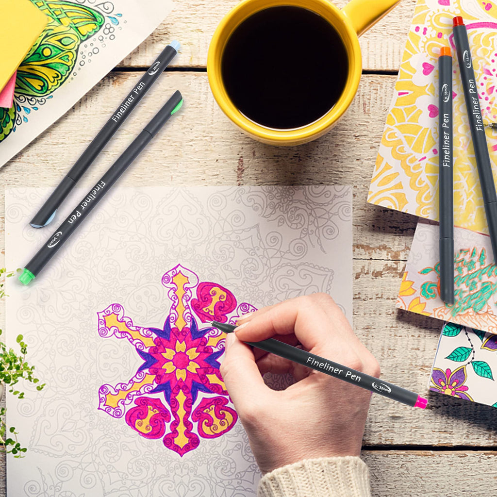 Hand coloring a mandala with fine liner pens, yellow mug of coffee nearby