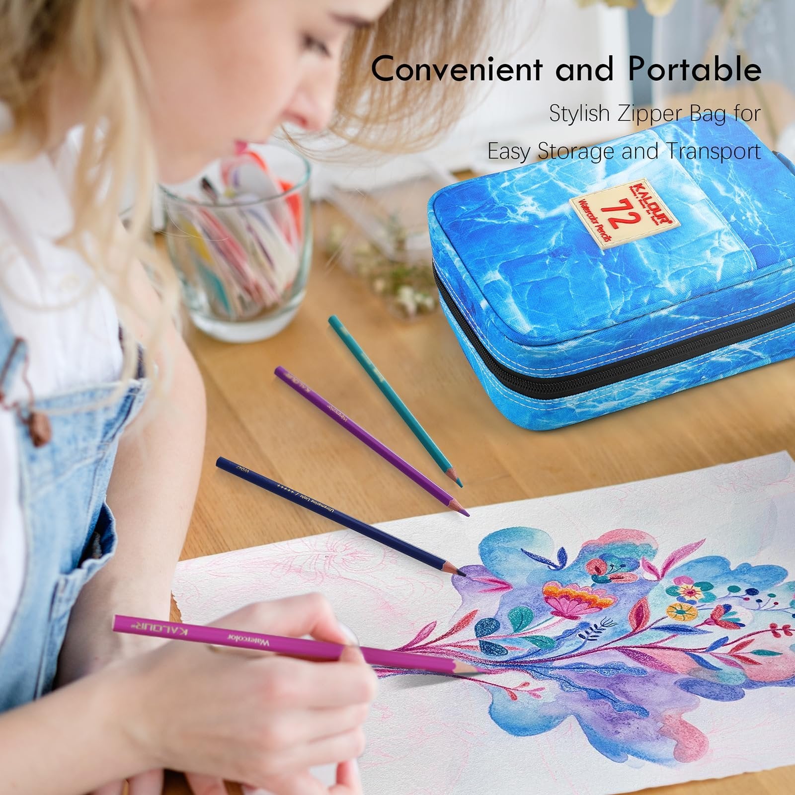 Woman drawing with watercolor pencils on paper, with a zippered pencil case and loose pencils on a wooden table.