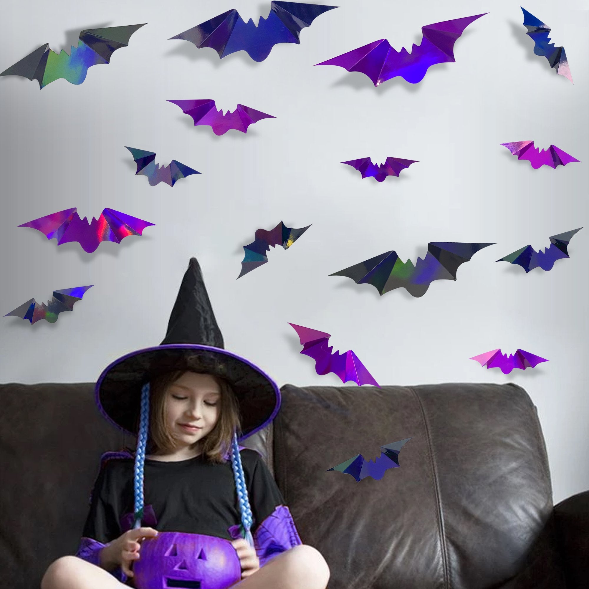 Girl in witch costume sitting on couch with holographic bat wall decals on wall behind her