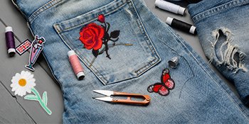 Embroidered iron-on patches including a rose, butterfly, and daisy, with spools of thread and scissors on denim jeans.