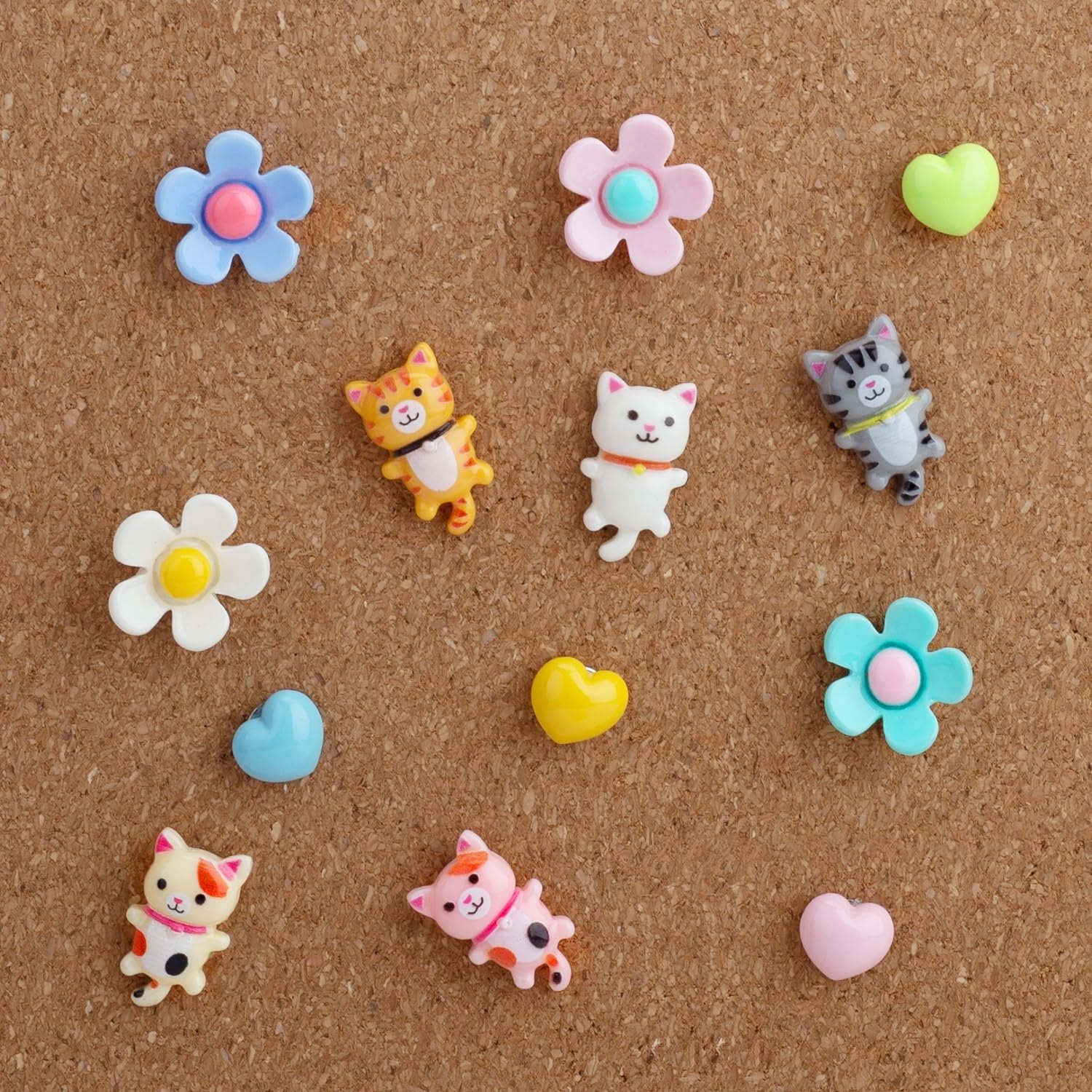 Assorted decorative push pins shaped like cats, flowers, and hearts on a corkboard.