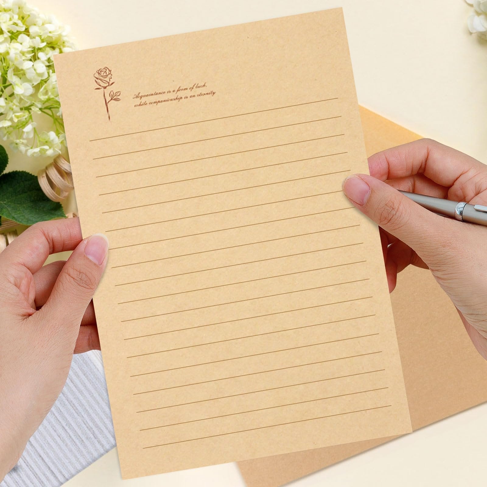 Hands holding a lined kraft paper with a rose illustration and quote, ready for writing.