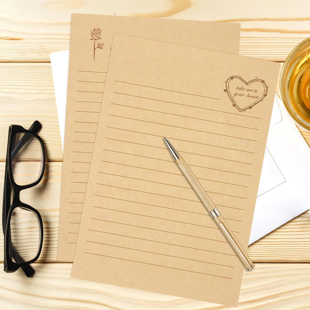 Vintage stationery set with lined kraft paper, pen, glasses, and a glass of amber liquid on a wooden desk.