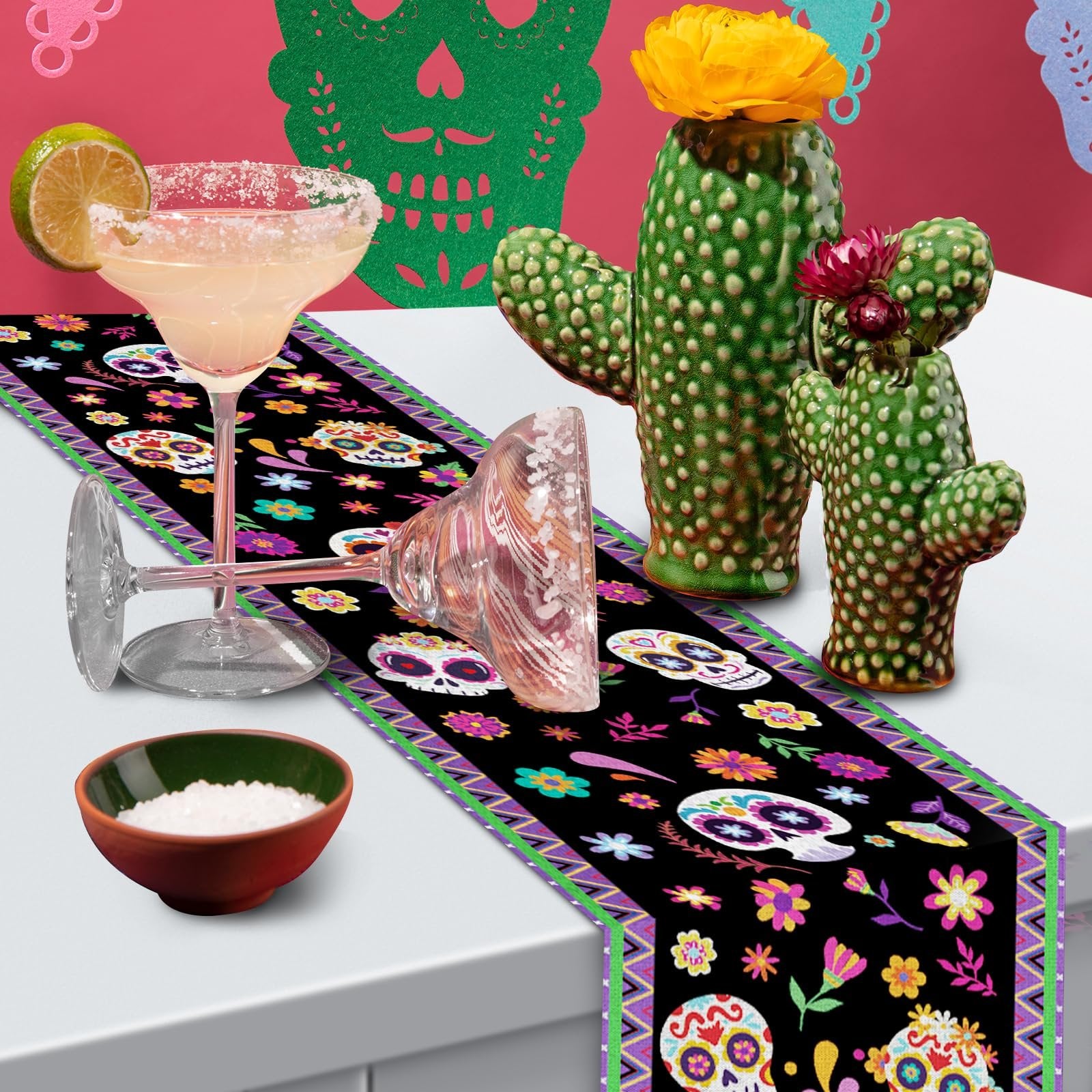 Day of the Dead table runner with sugar skull and floral print, set on a table with margarita glasses and cactus vases.