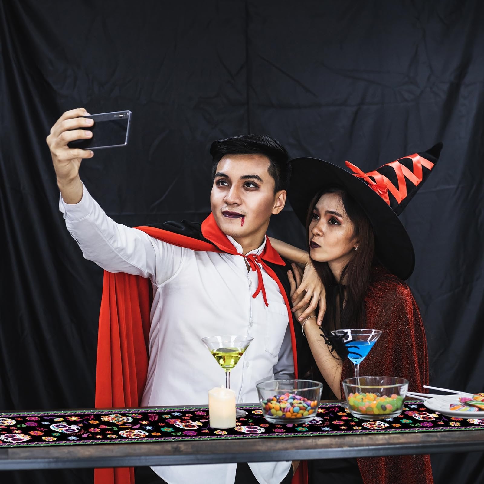 Couple in Halloween costumes taking a selfie at a table with a sugar skull print table runner