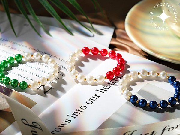 Three beaded bracelets with pearl and colored beads arranged on paper and fabric.