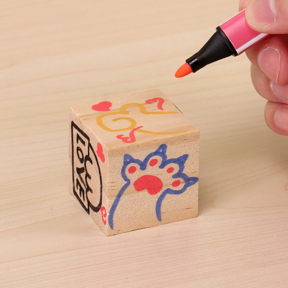 Wooden block with hand-drawn designs being decorated by an orange marker