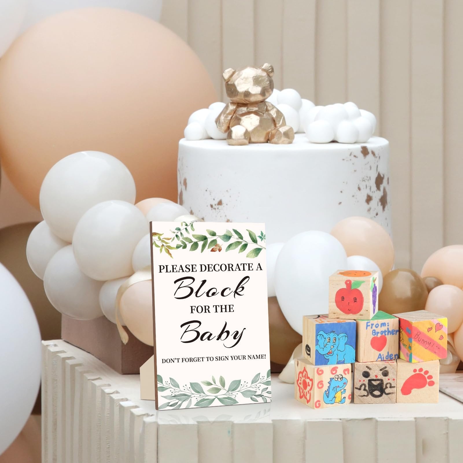 Baby shower block decorating station with a sign, decorated wooden blocks, and a cake with a teddy bear topper.