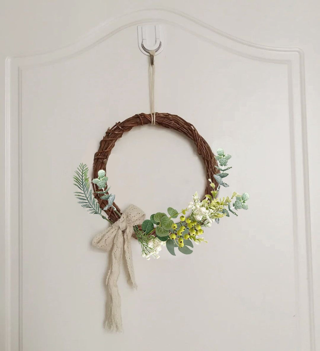 Woven wreath with artificial greenery and a cream ribbon bow, hanging on a white door.