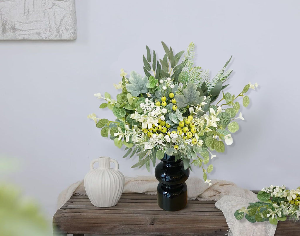 Artificial greenery stems with berries and white flowers in a black vase on a wooden surface