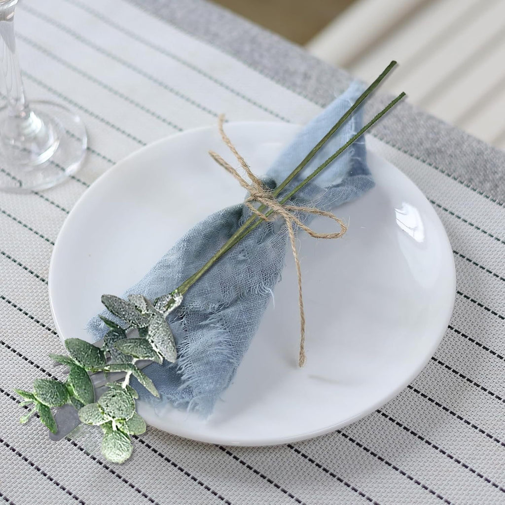 Artificial greenery stem with blue napkin tied with twine on a white plate