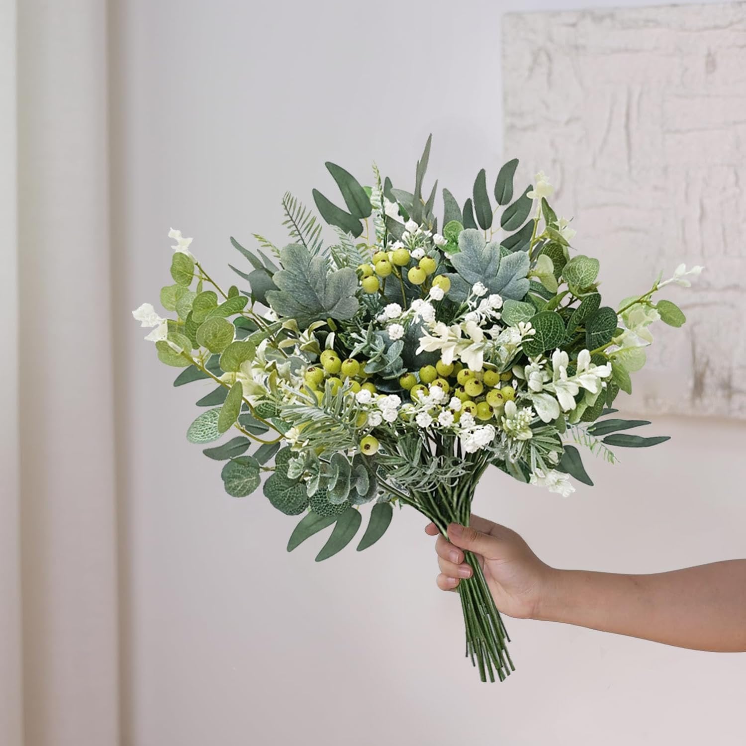 Hand holding a bouquet of artificial greenery stems with white flowers and yellow berries