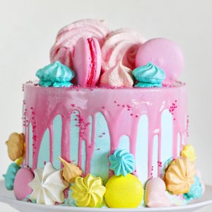 Decorated cake with pink drip icing, macarons, meringues, and sprinkles.