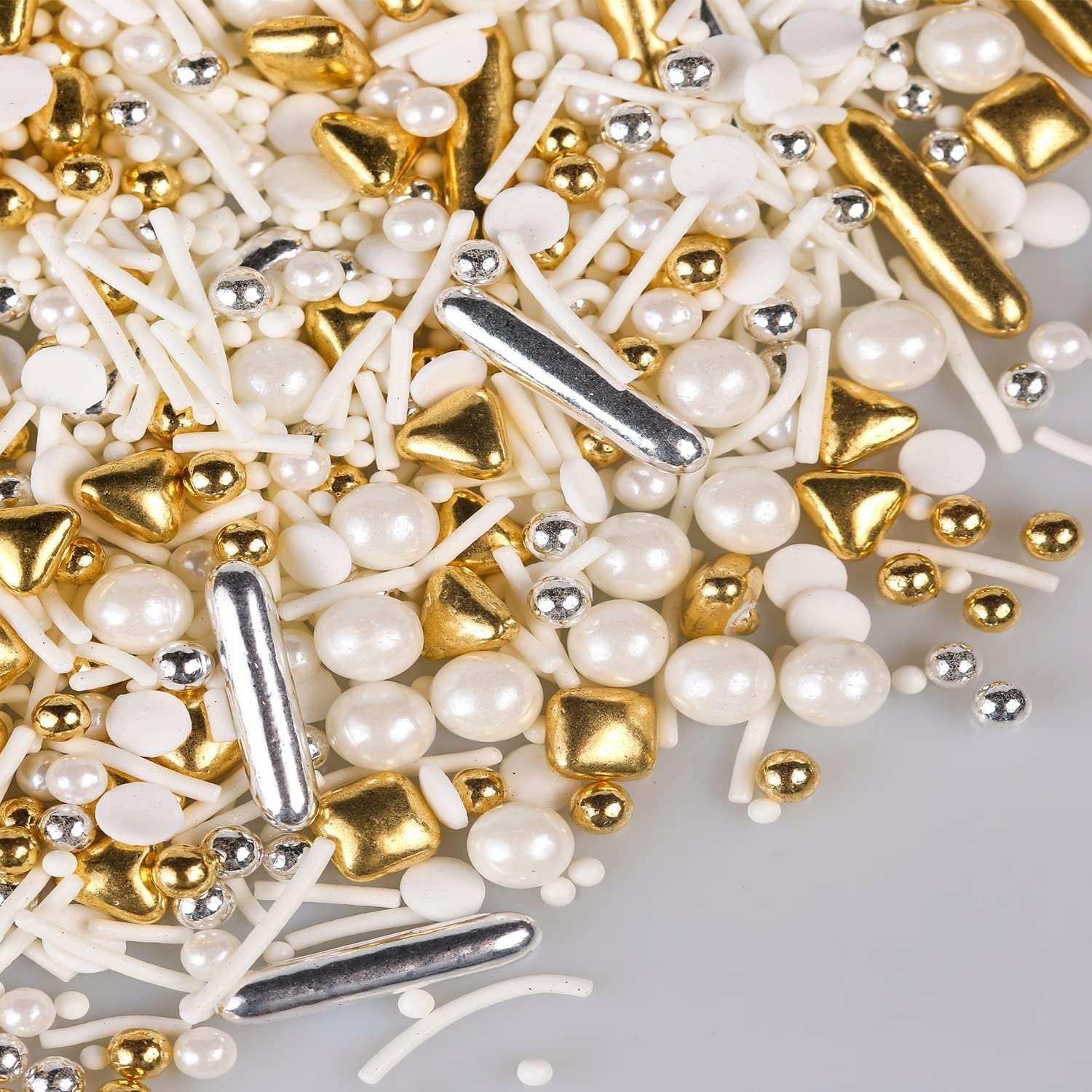 Close-up of gold, silver, and white cake sprinkles including pearls, rods, and balls on a light gray background.
